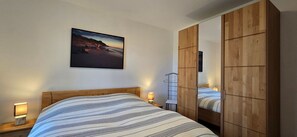 A bedroom with a bed, bedside lamps, a wooden wardrobe, and a framed picture on the wall.