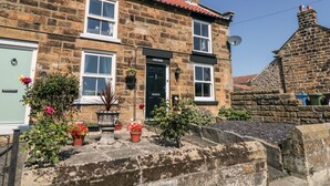 A stone building with a red-tiled roof, a green door, and a black front door. There are flower pots and a large urn on the front steps. - Puffin Cottage (Scarborough)