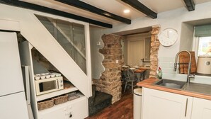 A compact kitchen with a wooden floor, white cabinets, a stone accent wall, and a clock on the wall. - Puffin Cottage (Scarborough)