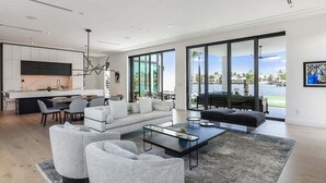 Ein modernes Wohnzimmer mit großem Fenster, Küchenzeile und einer Sitzecke mit Sofa und Sesseln.