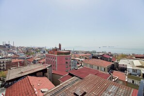 Eine Stadtansicht mit einem markanten Gebäude mit rotem Dach im Vordergrund und Blick auf das Meer im Hintergrund.