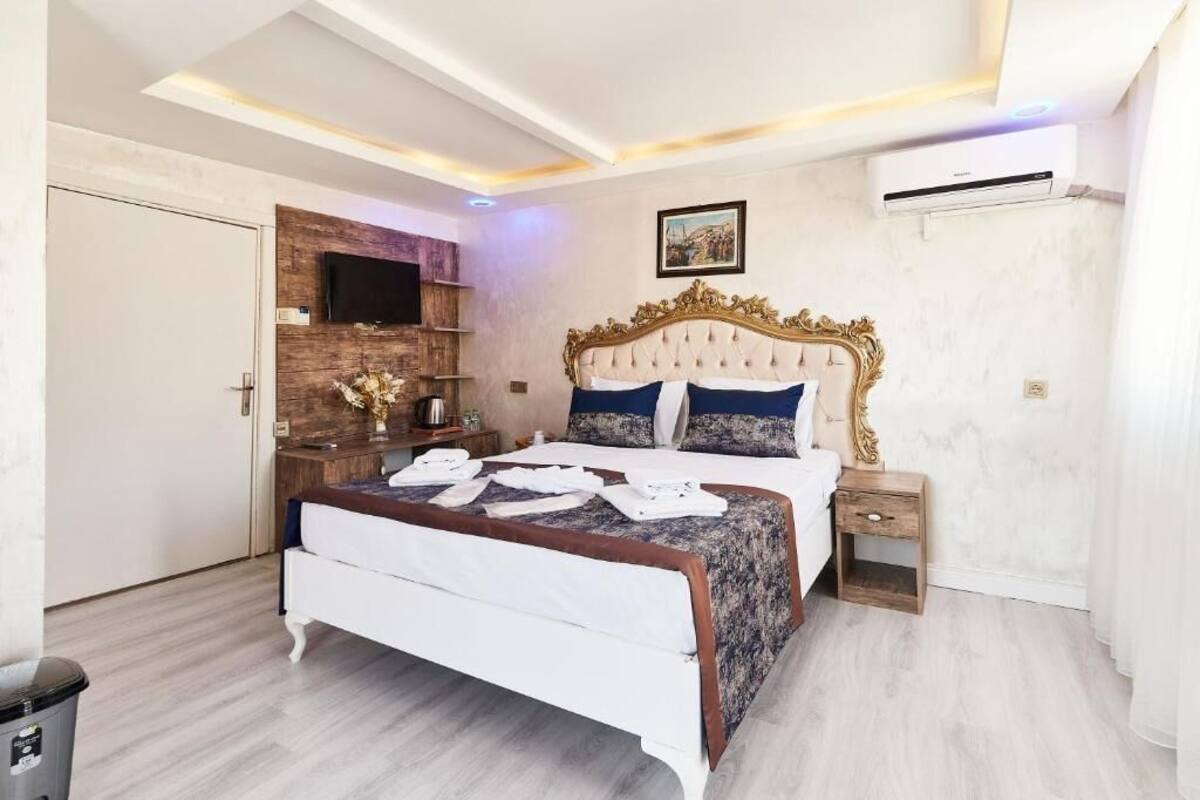A modern bedroom with a large bed, a wooden headboard, a mounted TV, and a small bedside table.