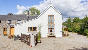 A two-story white building with a gravel driveway, wooden gate, and a small garden area with potted plants. - Drimnatorran Farm Lodge (Acharacle)