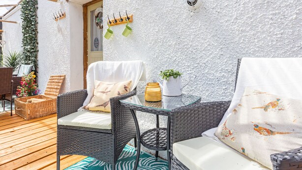 A patio with wicker furniture, a white textured wall, and a door with a heart decoration. - Drimnatorran Farm Lodge (Acharacle)