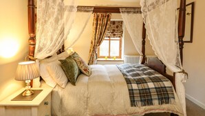 A four-poster bed with a canopy, a bedside table with a lamp, and a window with curtains. - Drimnatorran Farm Lodge (Acharacle)