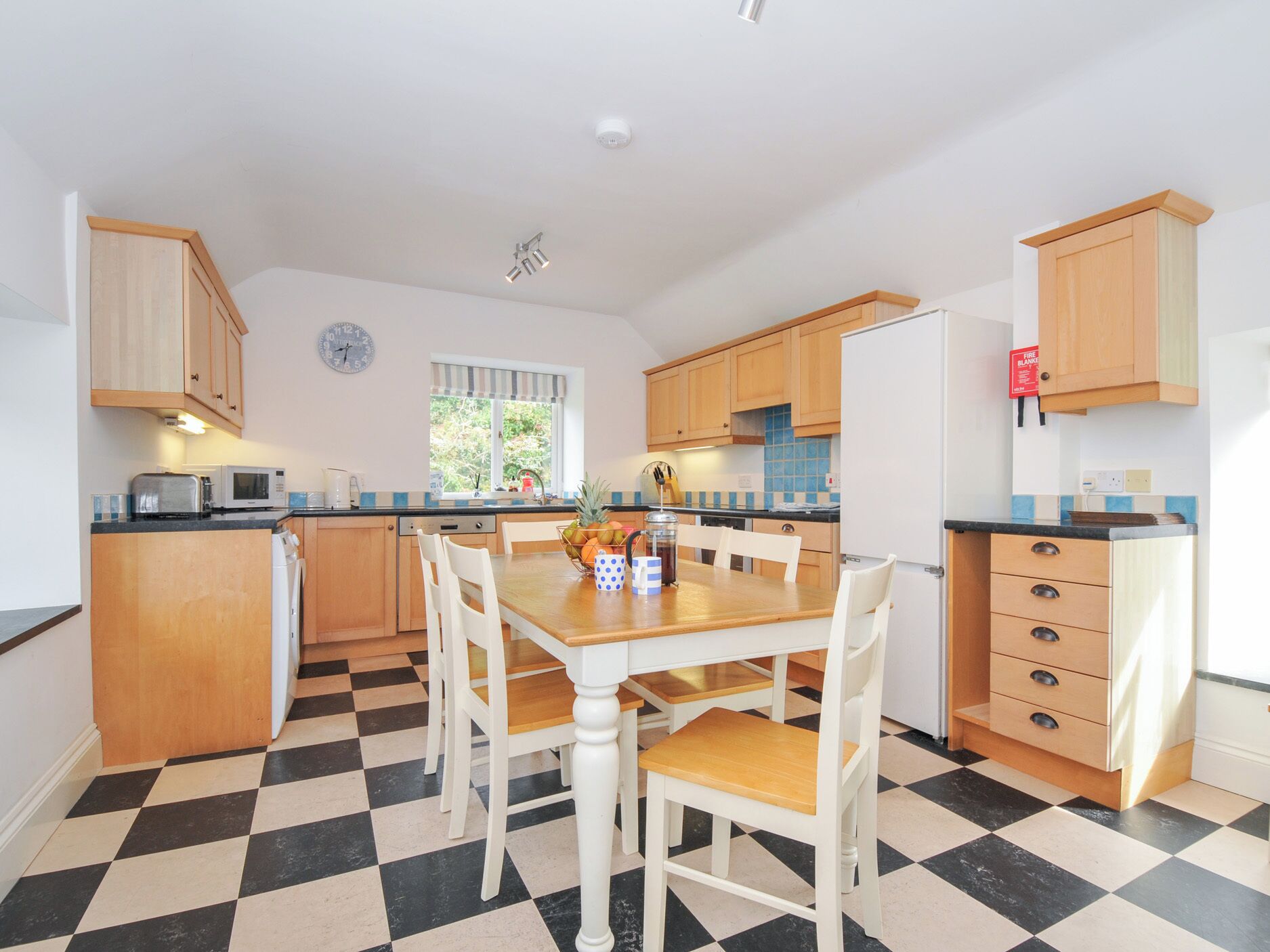 A kitchen with a checkered floor, wooden cabinets, a microwave, and a dining table with chairs.