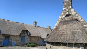 Un bâtiment en pierre avec un toit de chaume et une construction plus petite surmontée d’un toit conique.