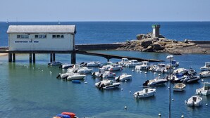 Un port de plaisance où sont amarrés de nombreux bateaux, un bâtiment blanc portant l’inscription « SAUVETAGE EN MER » sur un quai, et un phare en arrière-plan.