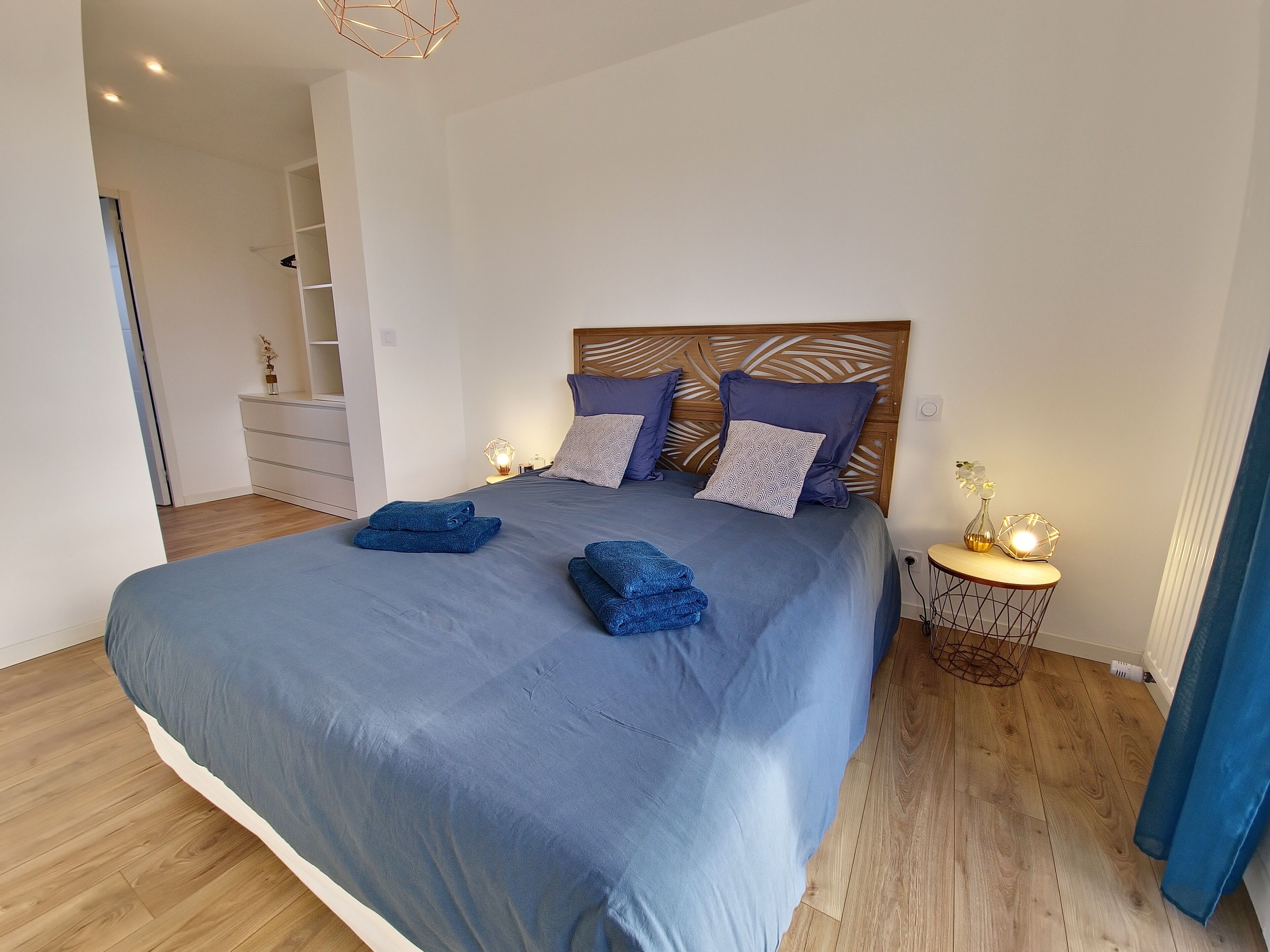 Un lit bien fait, avec une literie et des oreillers bleus, une tête de lit en bois et des lampes de chevet.
