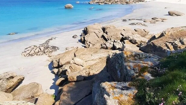 Une plage rocheuse bordée d’une eau d’un bleu limpide et d’une étendue de sable.