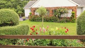 Una casa con fachada blanca, detalles de ladrillo y un jardín cuidado con diversas plantas y flores.