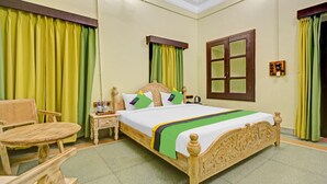 A neatly arranged bedroom with a bed, a chair, a nightstand, and a window with curtains. - Treebo The Regal House, Near Fateh Sagar Lake (Udaipur)