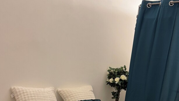 A bed with a white quilted bedspread, two white pillows, and two dark green pillows. A dark green throw blanket is draped over the foot of the bed. The room has wooden flooring and a blue curtain on the window. - Apartment terrace WIFI cable channels 4 pers Lille fac de droit Moulins (Lille)