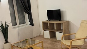 A living room with a glass coffee table, a television on a wooden stand, a beige armchair, a dark sofa, and a potted plant. - Apartment terrace WIFI cable channels 4 pers Lille fac de droit Moulins (Lille)