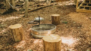 A rustic outdoor setting with a metal fire pit labeled "QUARRY COVE," surrounded by wooden stumps and a hammock.