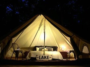 Una carpa con una cama en su interior, un letrero que dice 'LAKE' y un farol sobre una mesita.