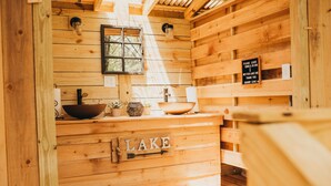A wooden cabin interior with a wooden sink, a window, and a sign that reads "PLEASE LEAVE TOWELS IN BIN THANK YOU QUARRY COVE".