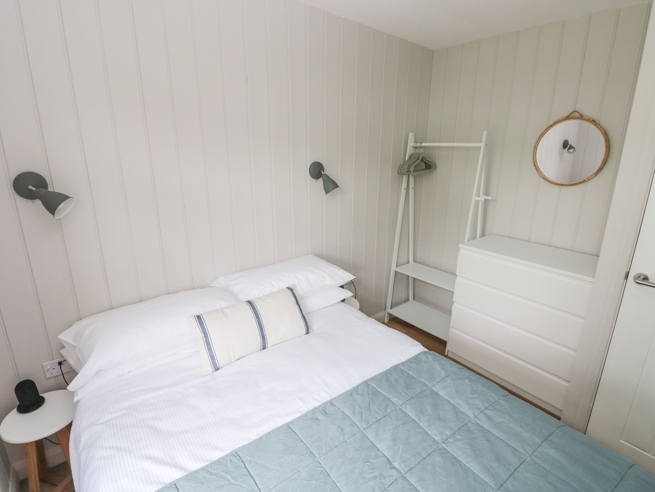 A neatly arranged bedroom with a bed, bedside tables, a dresser, and a wall-mounted mirror.
