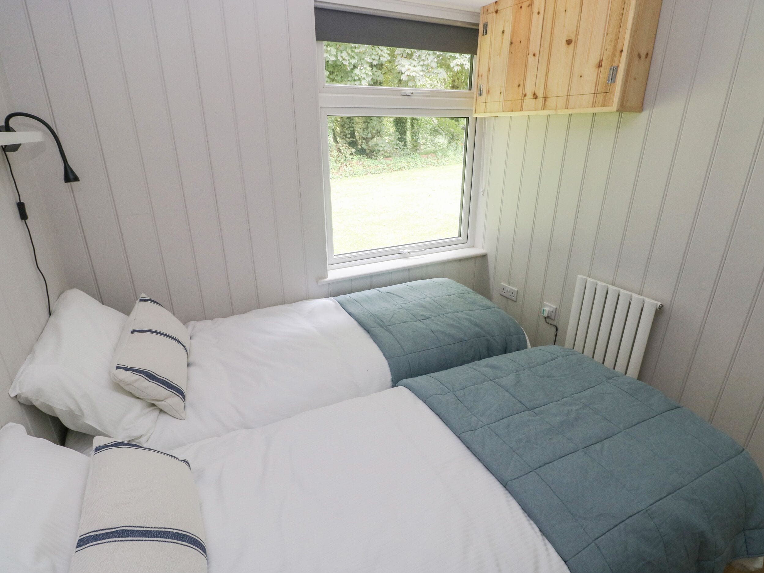 Een slaapkamer met twee bedden, een raam, een radiator en een houten kast boven het raam.