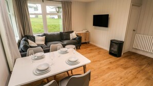 A modern living room with a dining table set for four, a sofa, a flat-screen TV, and a wood-burning stove. - Saltwater (Haverfordwest)