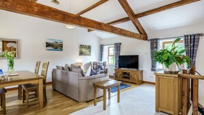 A spacious living room with a wooden dining table, sofa, and a television. - Ingleborough View (Carnforth)