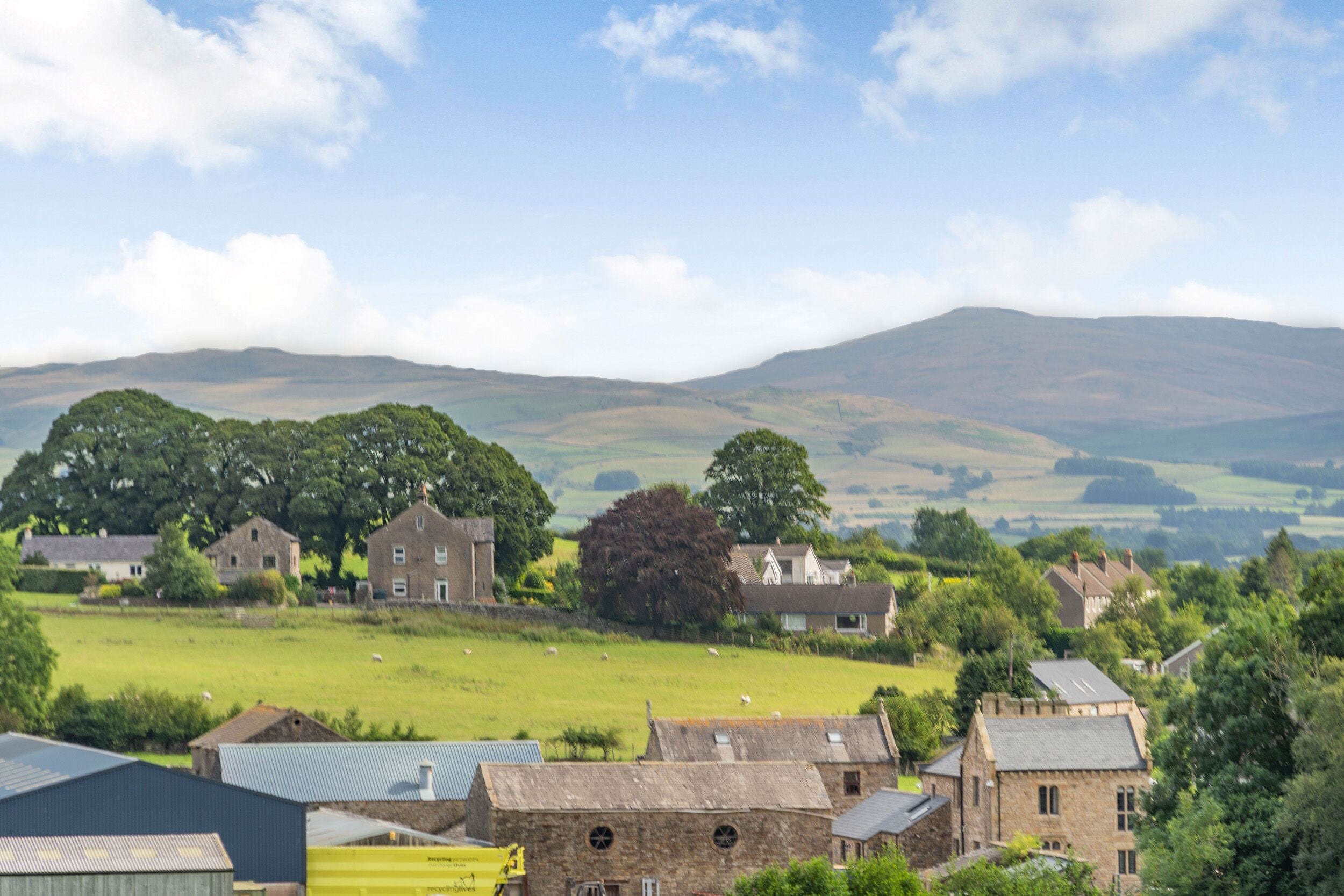 A rural village with stone buildings, green fields, and sheep grazing.