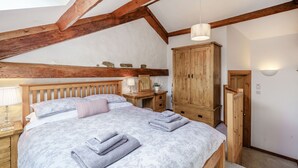 A bedroom with a wooden bed, a nightstand, a wooden wardrobe, and a ceiling with exposed beams. - Ingleborough View (Carnforth)