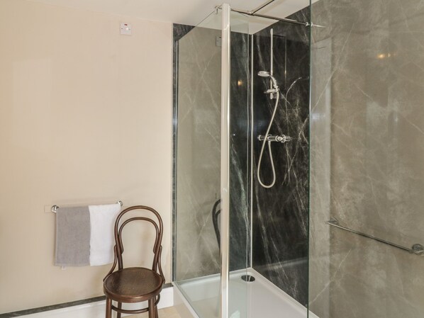 Un baño moderno con ducha de vidrio, una silla de madera y un perchero para toallas.