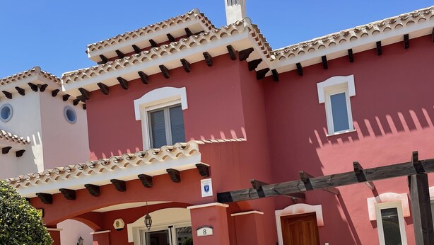A two-story building with a red facade, a covered patio area with a table and chairs, and a small garden. - Modern villa with private pool on 5 star Golf Resort (Torre-Pacheco)