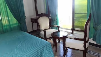 Habitación de hotel con cama, dos sillas, una mesita, un espejo y vistas a zonas verdes por la ventana.