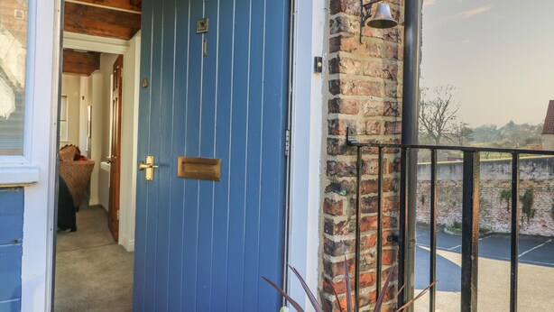 A blue door with a brass handle and a small brass plate, a brick wall, and a metal railing. - 1 Rodgers Mews (Malton)