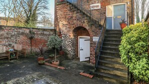 A two-story brick building with a white door, a blue window, and a staircase leading to the upper floor. - 1 Rodgers Mews (Malton)
