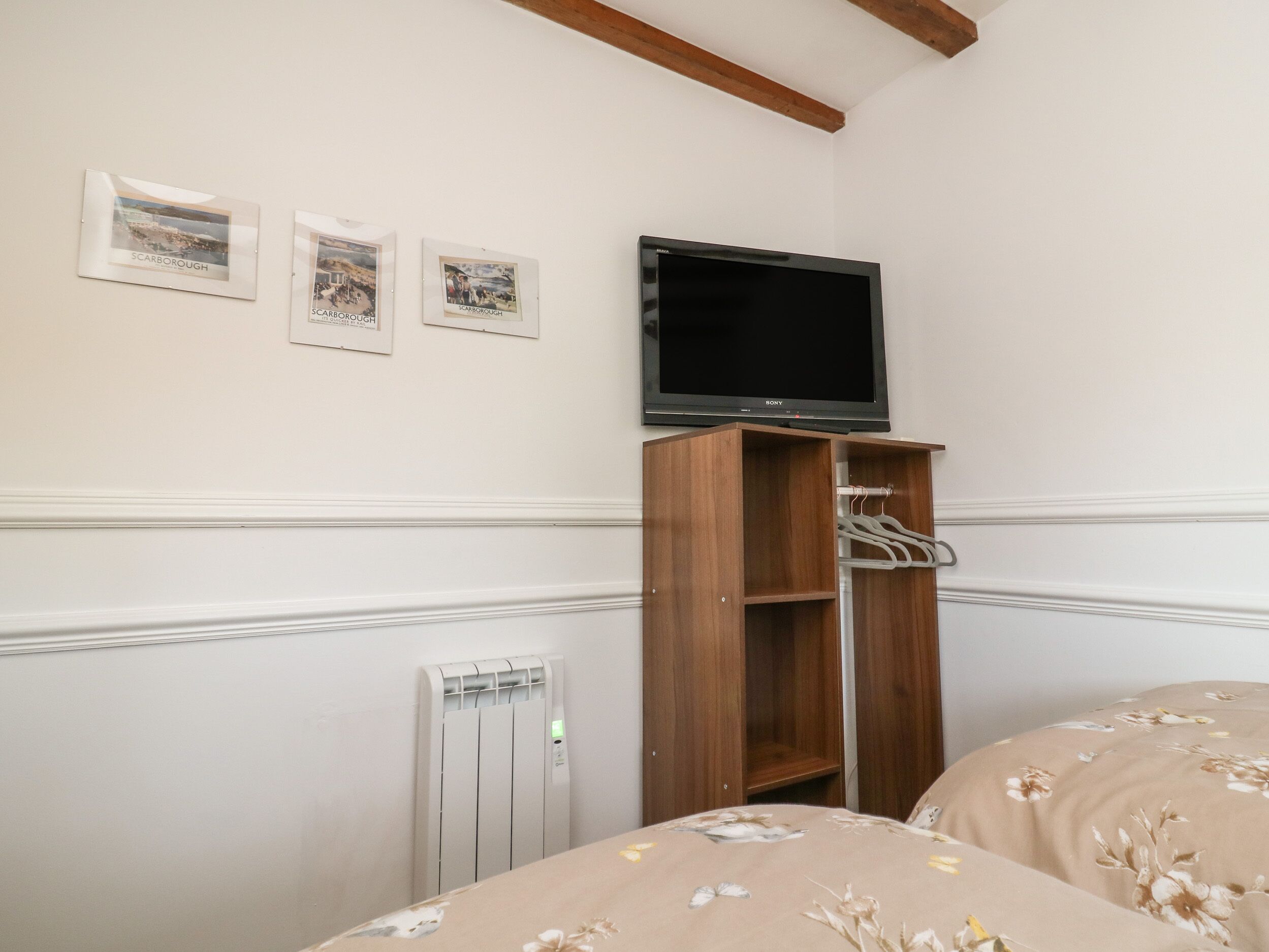 Une chambre à coucher comprenant un lit, une armoire en bois, un téléviseur fixé au mur et un radiateur.