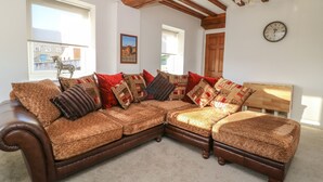 A L-shaped sectional sofa with multiple patterned cushions, a wooden headboard, and a clock on the wall. - 1 Rodgers Mews (Malton)