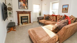 A living room with a fireplace, a sofa set, a television, and decorative items on shelves. - 1 Rodgers Mews (Malton)