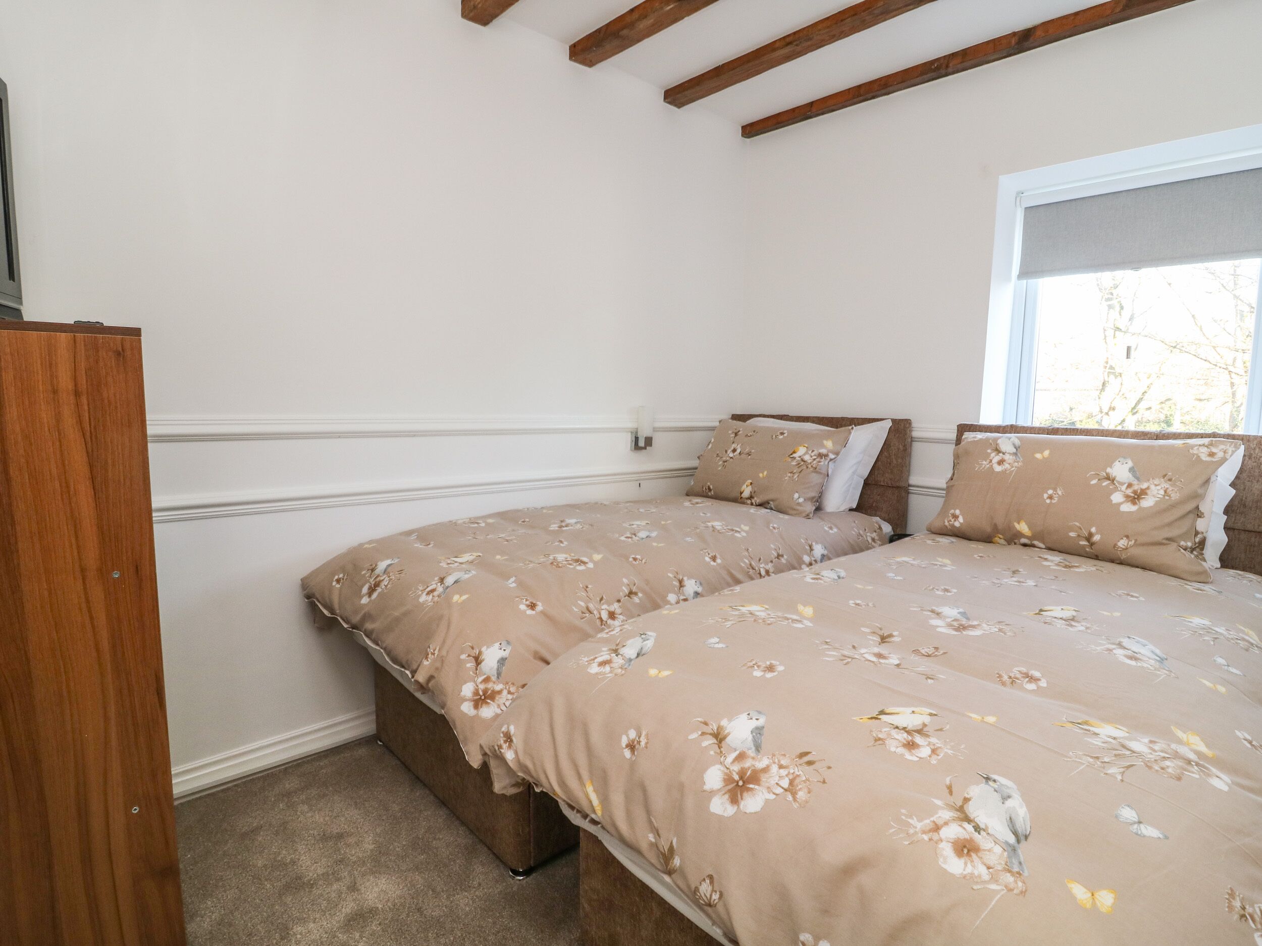 A bedroom with two beds, a wooden wardrobe, and a window with a view of trees.