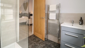 A modern bathroom with a glass shower enclosure, a wooden door, a towel rack, a sink, and a bottle of hand soap.