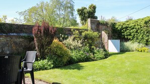 A garden with a stone wall, a white gate, and a chair. - The Stables (Shrewsbury)