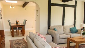 A living room with a sofa set, a coffee table, and a dining area with a table and chairs. - The Stables (Shrewsbury)