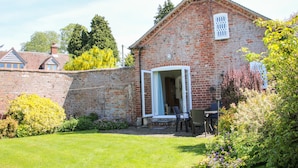A brick house with a garden, a dining area with chairs, and a window with a white frame. - The Stables (Shrewsbury)