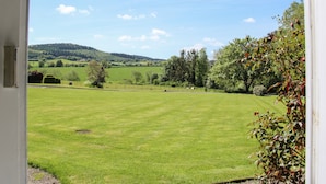 A view from a window of a grassy field with a fence, trees, and hills in the distance. - The Stables (Shrewsbury)