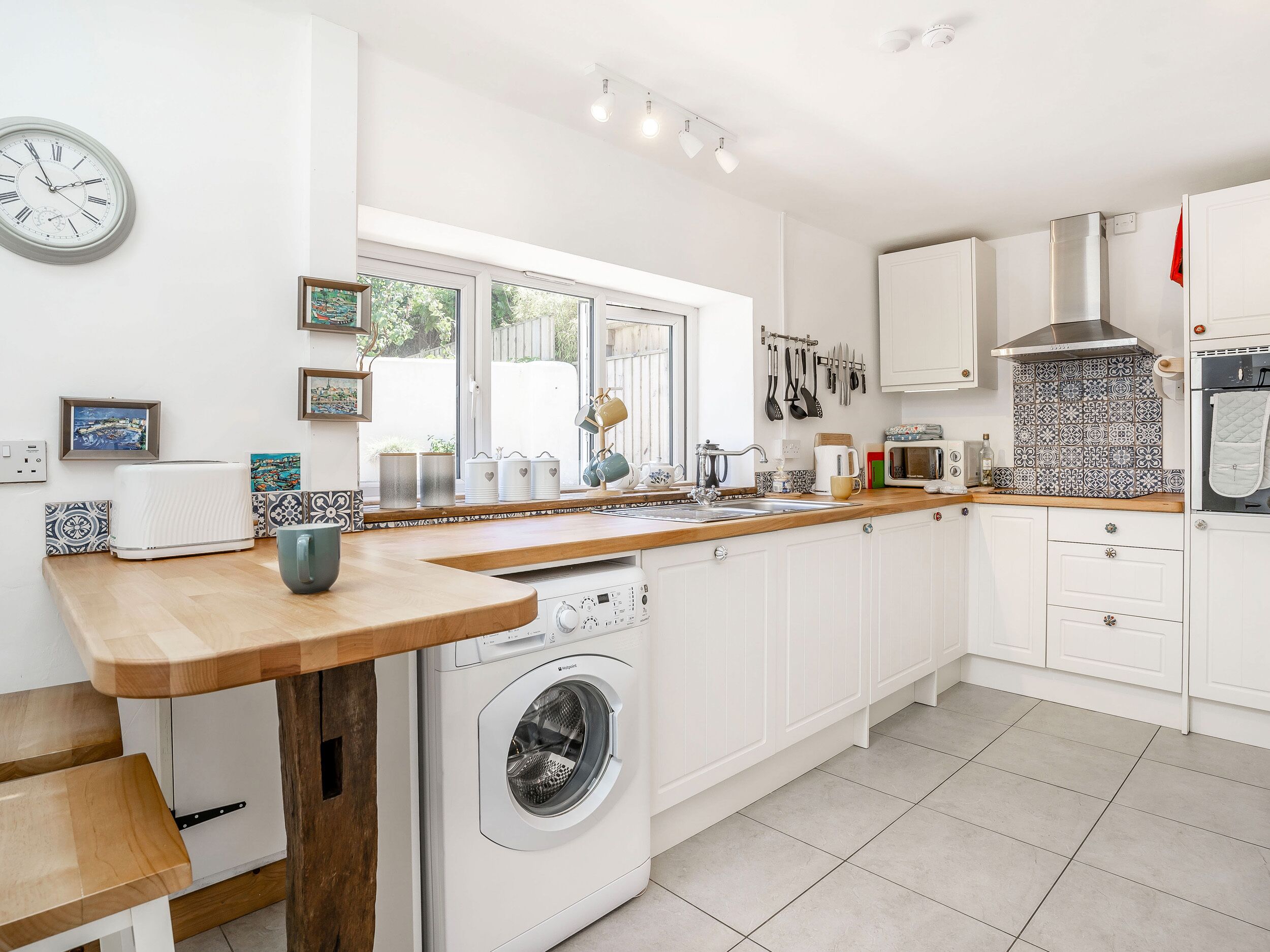 A modern kitchen with white cabinetry, a built-in washing machine, a wooden countertop, and a large window providing natural light.