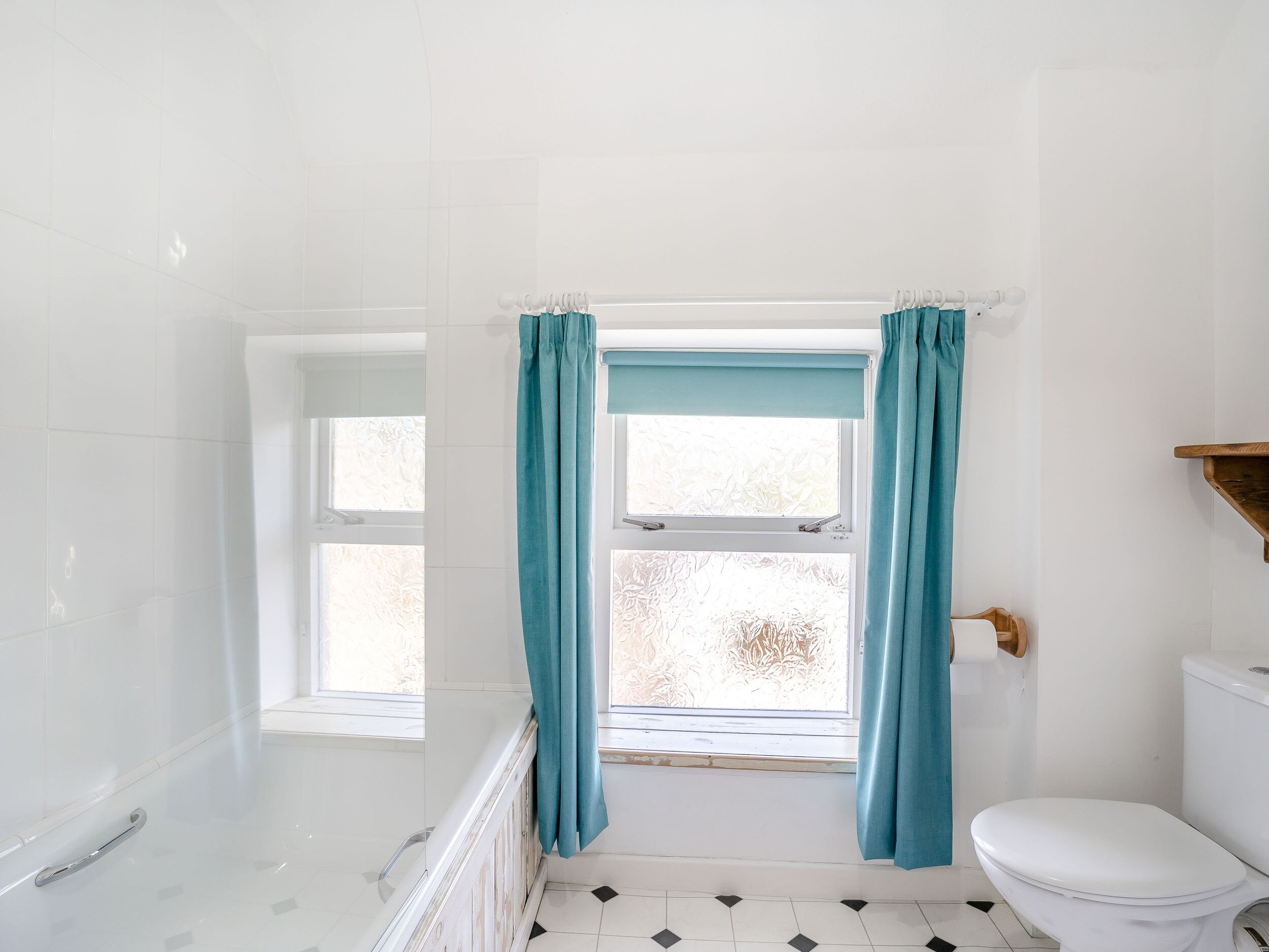 A bathroom with a bathtub, toilet, and a window with curtains.