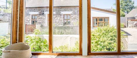 A room with a large window overlooking a stone building and greenery.