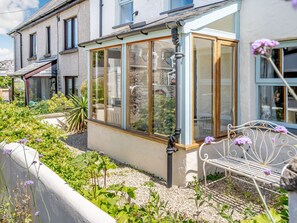 Une maison avec une véranda, un jardin avec différentes espèces de plantes et un banc.