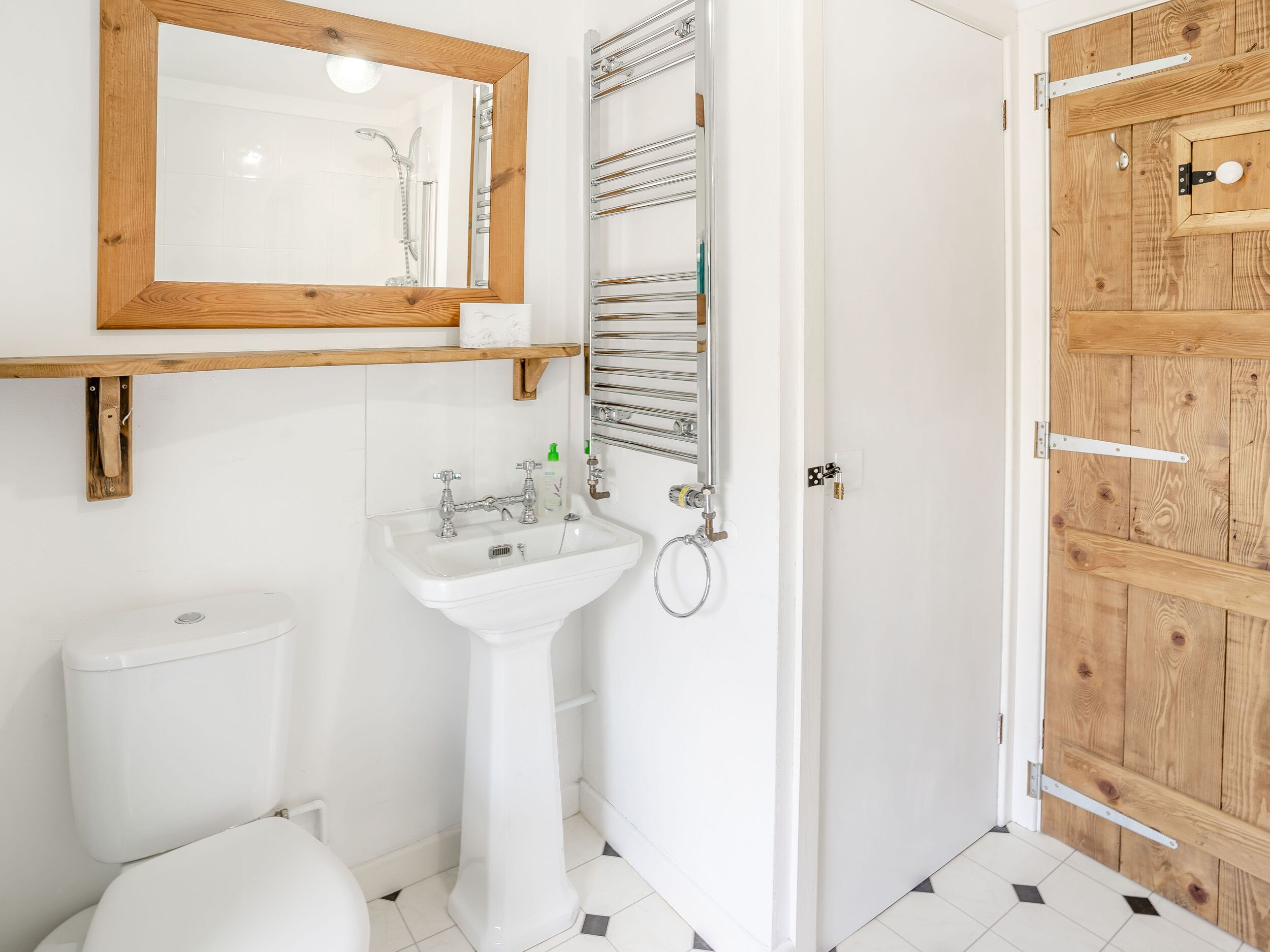 Un baño con puerta de madera, un lavamanos blanco, un inodoro y un espejo con marco de madera.