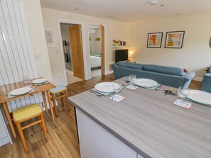 A modern kitchen with a dining table set for four, a grey countertop, and a blue sofa in the background. - 2 The Villa (Ludlow)