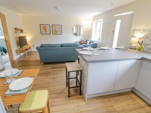 A modern kitchen with white cabinets, a central island, and a dining area with a wooden table and chairs. - 2 The Villa (Ludlow)