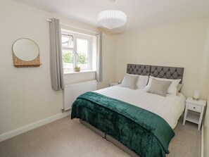 A bedroom with a bed, a nightstand, a bedside lamp, a window with curtains, a radiator, and a wall-mounted mirror. - 2 The Villa (Ludlow)