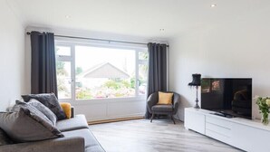 A modern living room with a grey sofa, a white entertainment unit, and a television. - Greenaway, 4 Rockhaven Gardens (Wadebridge)